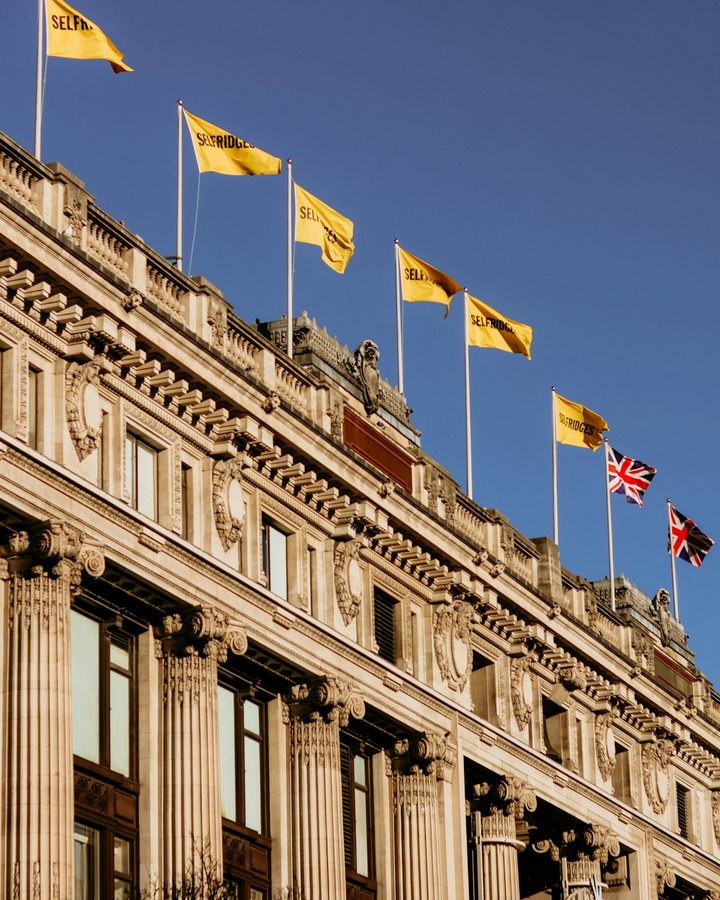 The roofline of Selfridges on Oxford Street, its yellow flags against a blue sky