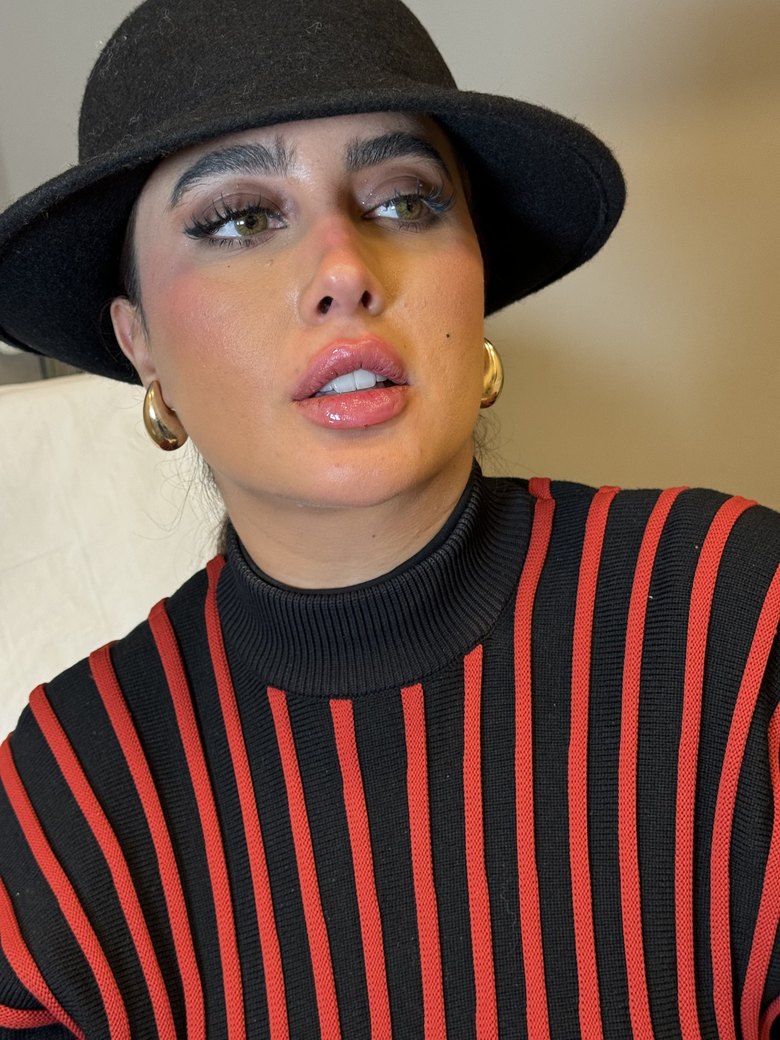Aldanah Beauty in a black hat and gold earrings, looking up past the camera