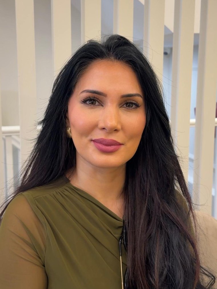 Sadia Khan smiling at the clinic, her long dark hair over an olive green top